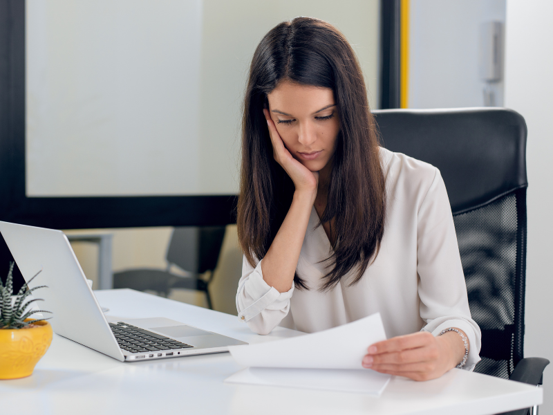 A woman resting her chin on her hand reads a document