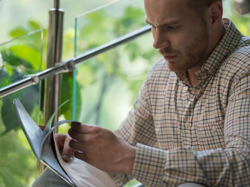 A man sitting on the stairs reads documents with a worried expression, reading about tax debts to the ATO