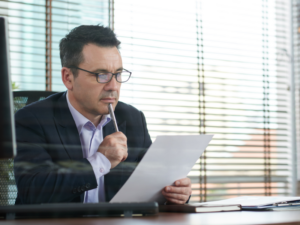 A man in his office reading a document with a pen against his chin, a business owner reviewing an ATO notice