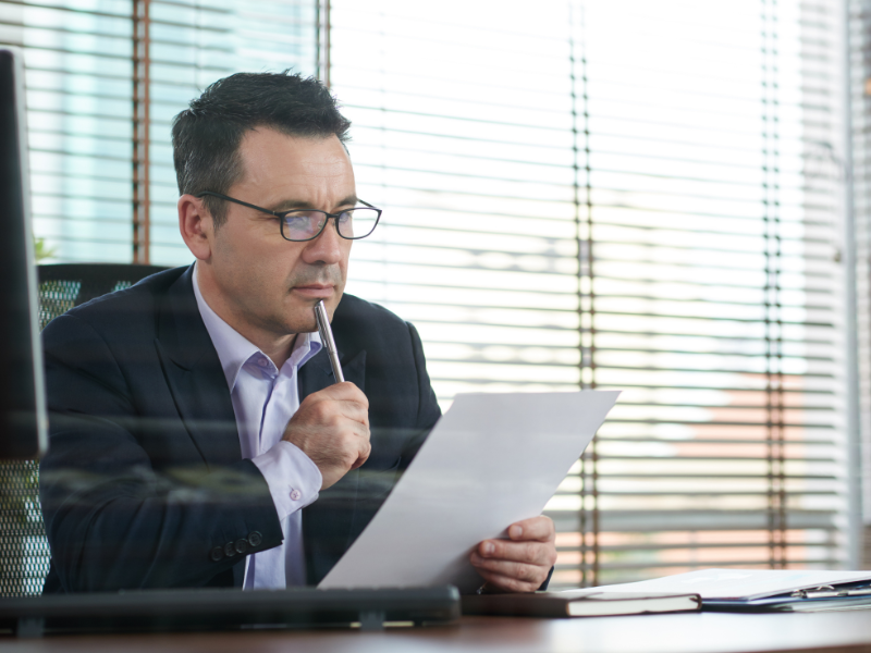 A man in his office reading a document with a pen against his chin, a business owner reviewing an ATO notice