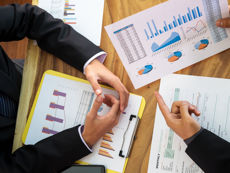 Cropped photo of two people discussing the growth of their business, pointing to documents with charts, top view photo