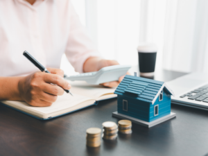 Cropped photo of a business owner calculating how much they can borrow based on property equity, a miniature house and piles of coins on the table