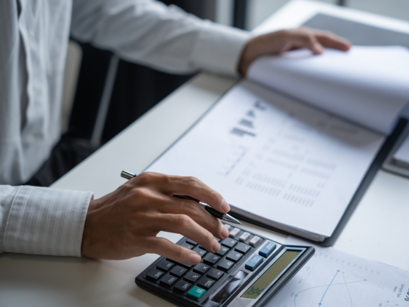 Cropped photo of a man using a calculator while reviewing documents, business owner calculating the cost of a business line of credit