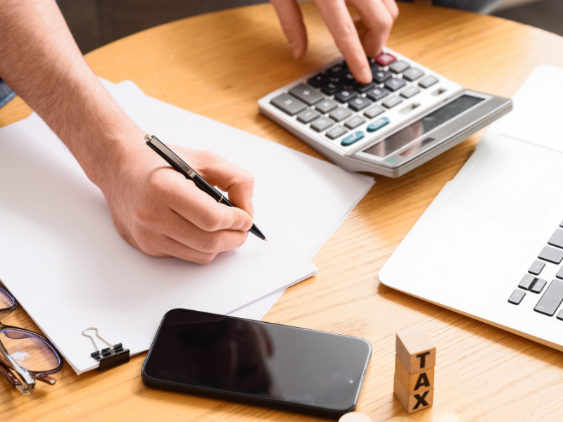 Cropped photo of a man using a calculator and writing on documents, man calculating how much he owes in penalties for not lodging BAS on time