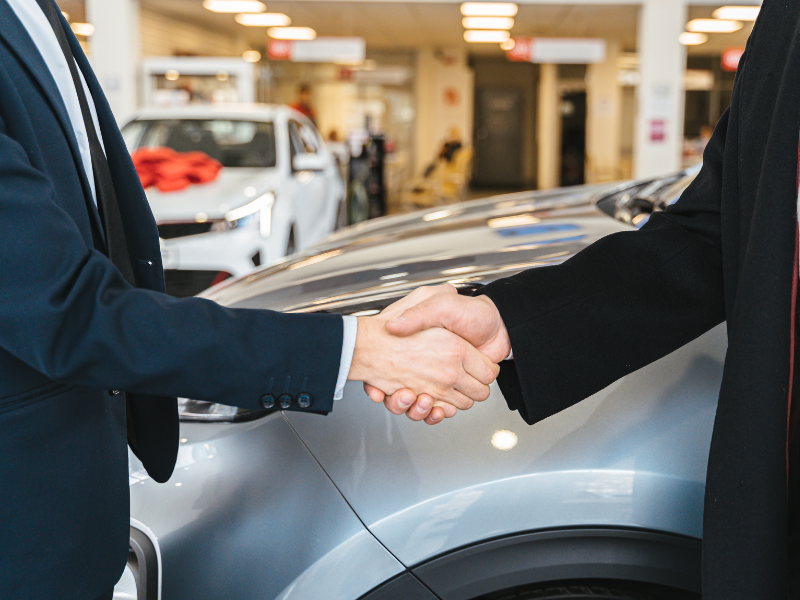 A car salesman and a customer shake hands at a car dealership