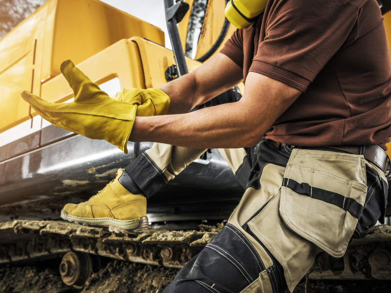 Cropped photo of an equipment operator sitting on the tracks of his equipment, putting on safety gloves