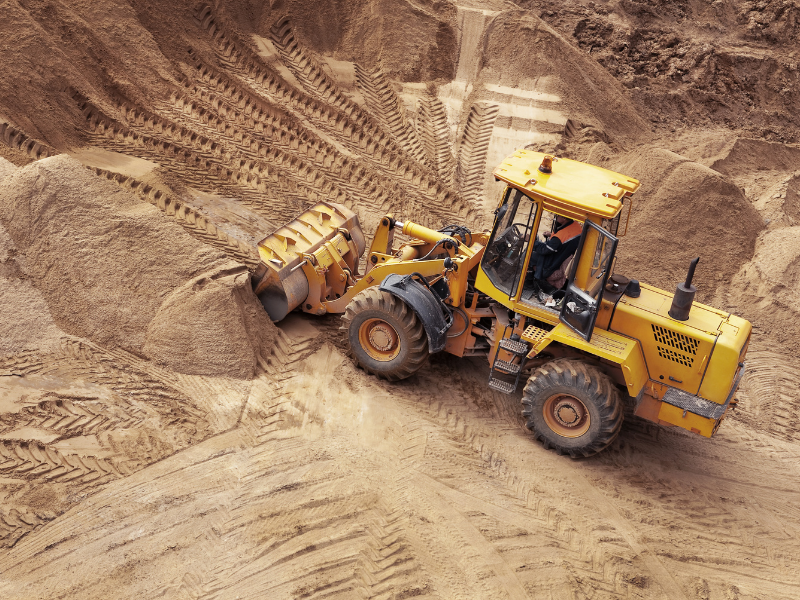 A small wheeled bulldozer driving over dirt, equipment wheel tracks all over the surface of the dirt