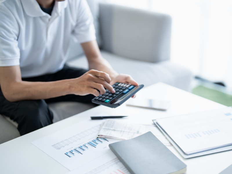 Cropped photo of a man using a calculator, documents and a notebook on the table